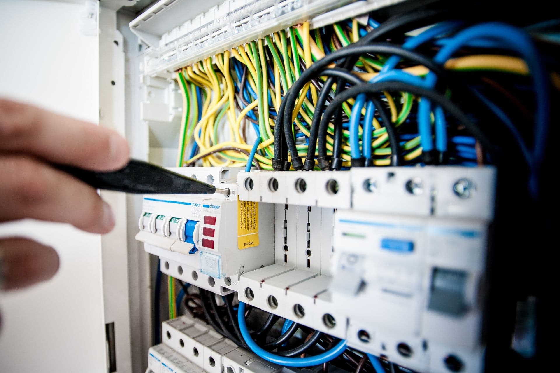 An electrician working on an open switchboard with circuit breakers and wiring.